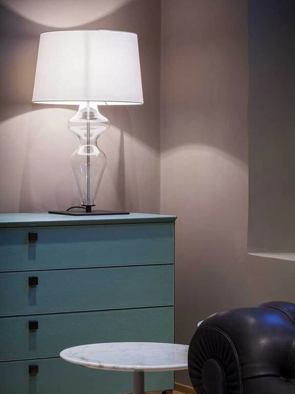 Lampada da tavolo Holly Desk Lamp con paralume in tessuto e base formata da una sagoma in vetro trasparente dalle linee morbide e slanciate con base d’appoggio in metallo di Poltrona Frau